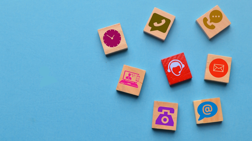 Auf einer blauen Fläche liegen Holzklötze, die mit verschiedenen Icons, z. B. Telefonhörern, Headsets, Mail-Symbolen und Laptops, verziert sind. Auf einer blauen Fläche liegen Holzklötze, die mit verschiedenen Icons, z. B. Telefonhörern, Headsets, Mail-Symbolen und Laptops, verziert sind.