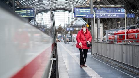 Sehbehinderte Reisende ertastet mit Langstock den Leitstreifen des Bodenleitsystems auf dem Bahnsteig im Hbf Frankfurt am Main