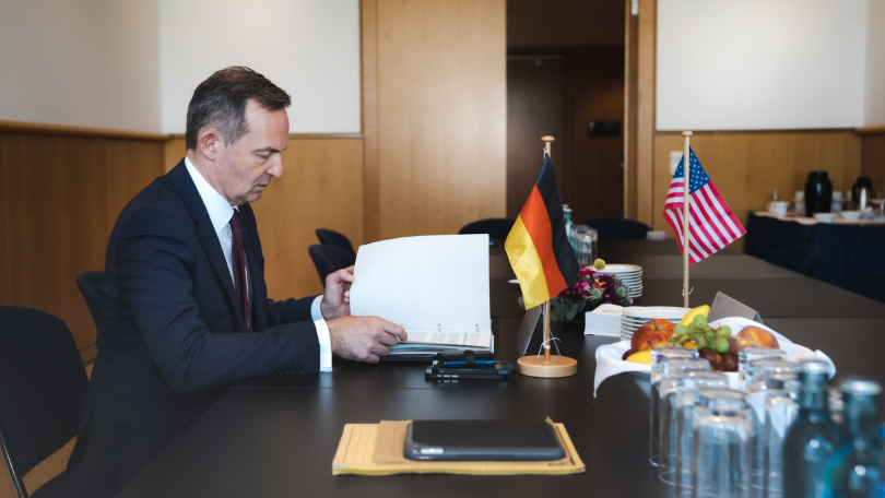Bundesminister Dr. Volker Wissing beim Weltverkehrsforum 2022. Der Minister sitzt an einem Konferenztisch und liest Dokumente. Auf dem Tisch stehen die deutsche und die US-amerikanische Flagge sowie eine Obstschale und mehrere Gläser. Bundesminister Dr. Volker Wissing beim Weltverkehrsforum 2022. Der Minister sitzt an einem Konferenztisch und liest Dokumente. Auf dem Tisch stehen die deutsche und die US-amerikanische Flagge sowie eine Obstschale und mehrere Gläser.