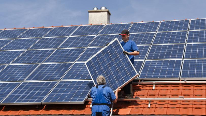 Zwei Arbeiter montieren eine Photovoltaik-Anlage auf dem Dach eines Hauses