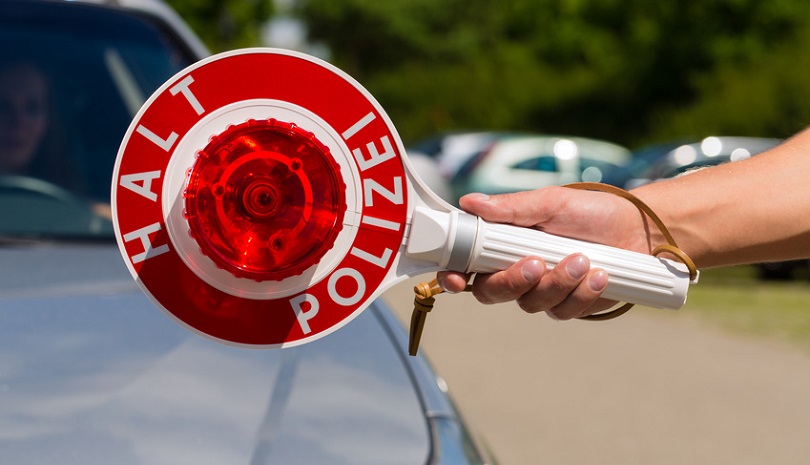 Autos im Hintergrund, im Vordergrund ein Arm der eine Polizeikelle in der Hand hält Autos im Hintergrund, im Vordergrund ein Arm der eine Polizeikelle in der Hand hält