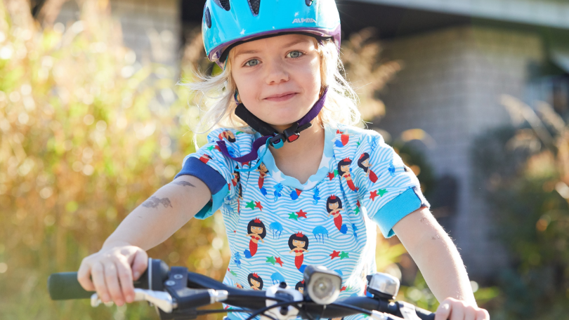 Ein Kind mit Fahrradhelm sitzt auf einem Fahrrad und blickt lächelnd in die Kamera Ein Kind mit Fahrradhelm sitzt auf einem Fahrrad und blickt lächelnd in die Kamera