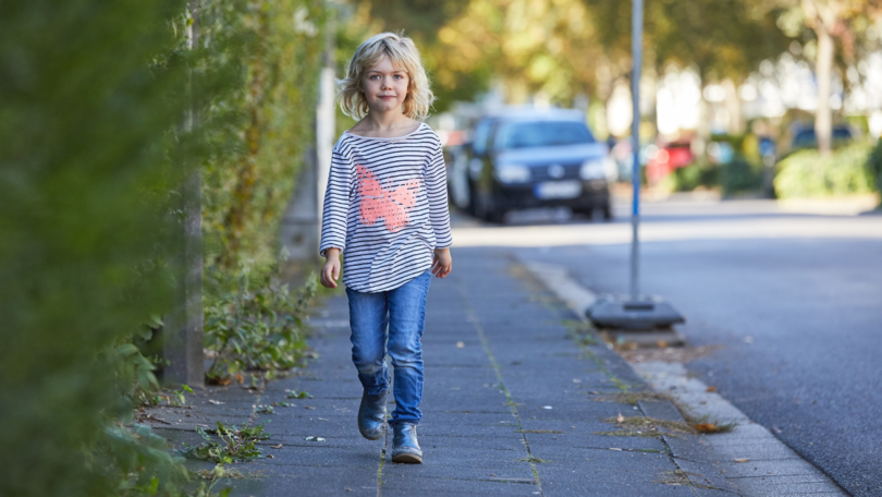Ein Kind geht auf dem Gehweg einer Straße Ein Kind geht auf dem Gehweg einer Straße